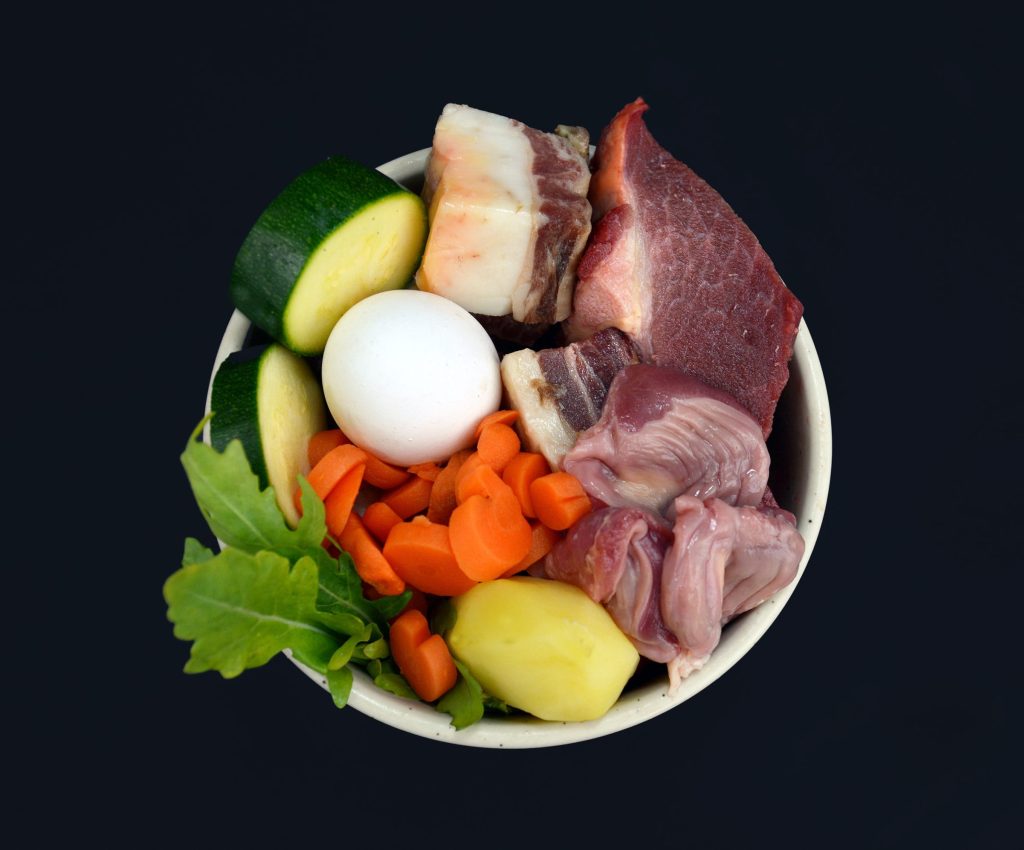 Bowl of mixed food items including eggs, meat and vegetables on a black background